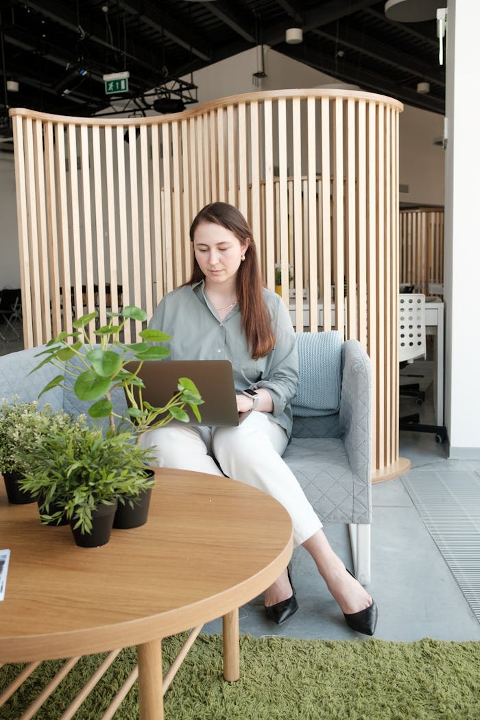 ours-journey A woman working on a laptop in a modern office with plants and wooden dividers.